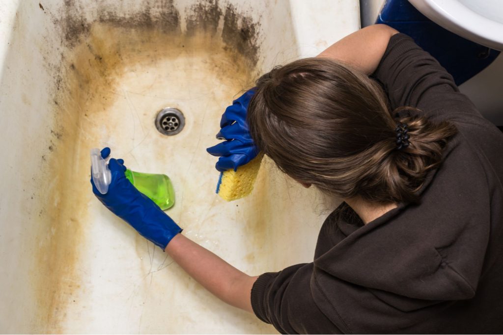 A woman diligently cleaning a stained tub with a sponge, representing a bathroom mold removal service in Joliet, IL.