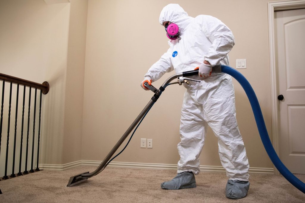 Wearing a white suit and protective gear, a person vacuums carpet mold in Joliet, IL, as part of a removal service.