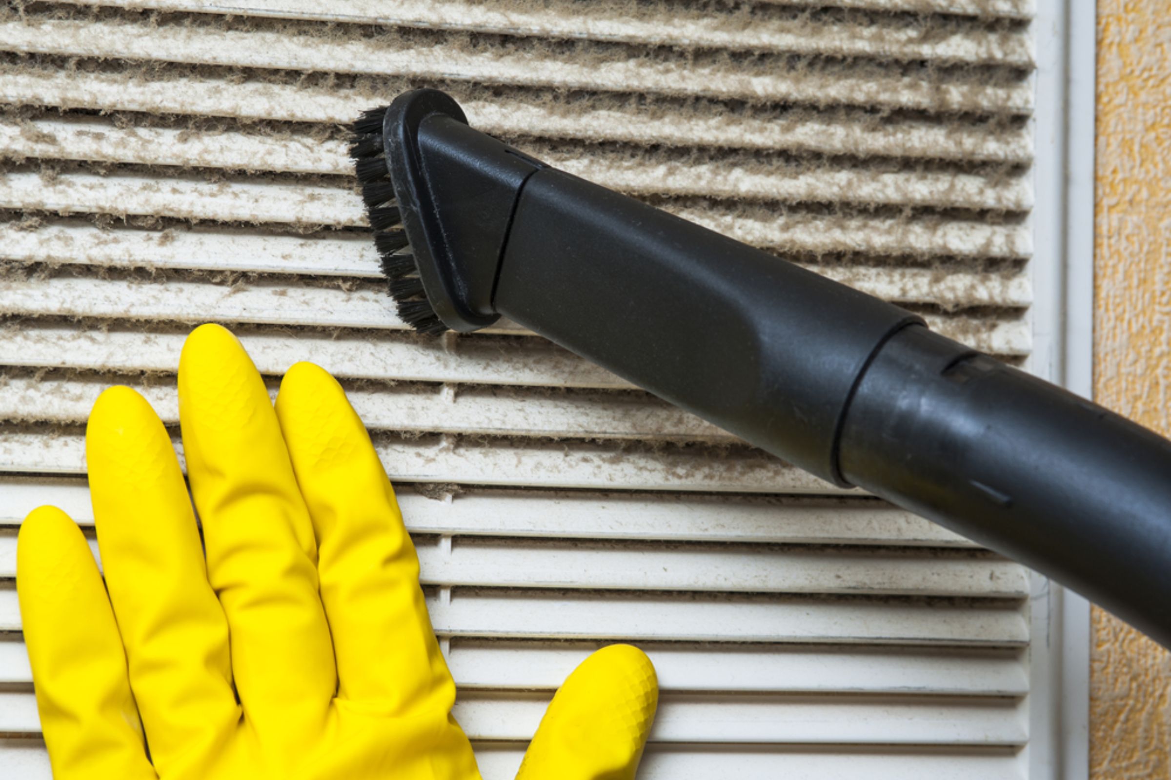 Individual wearing yellow gloves uses a vacuum cleaner for mold removal in an HVAC service setting in Joliet, IL.