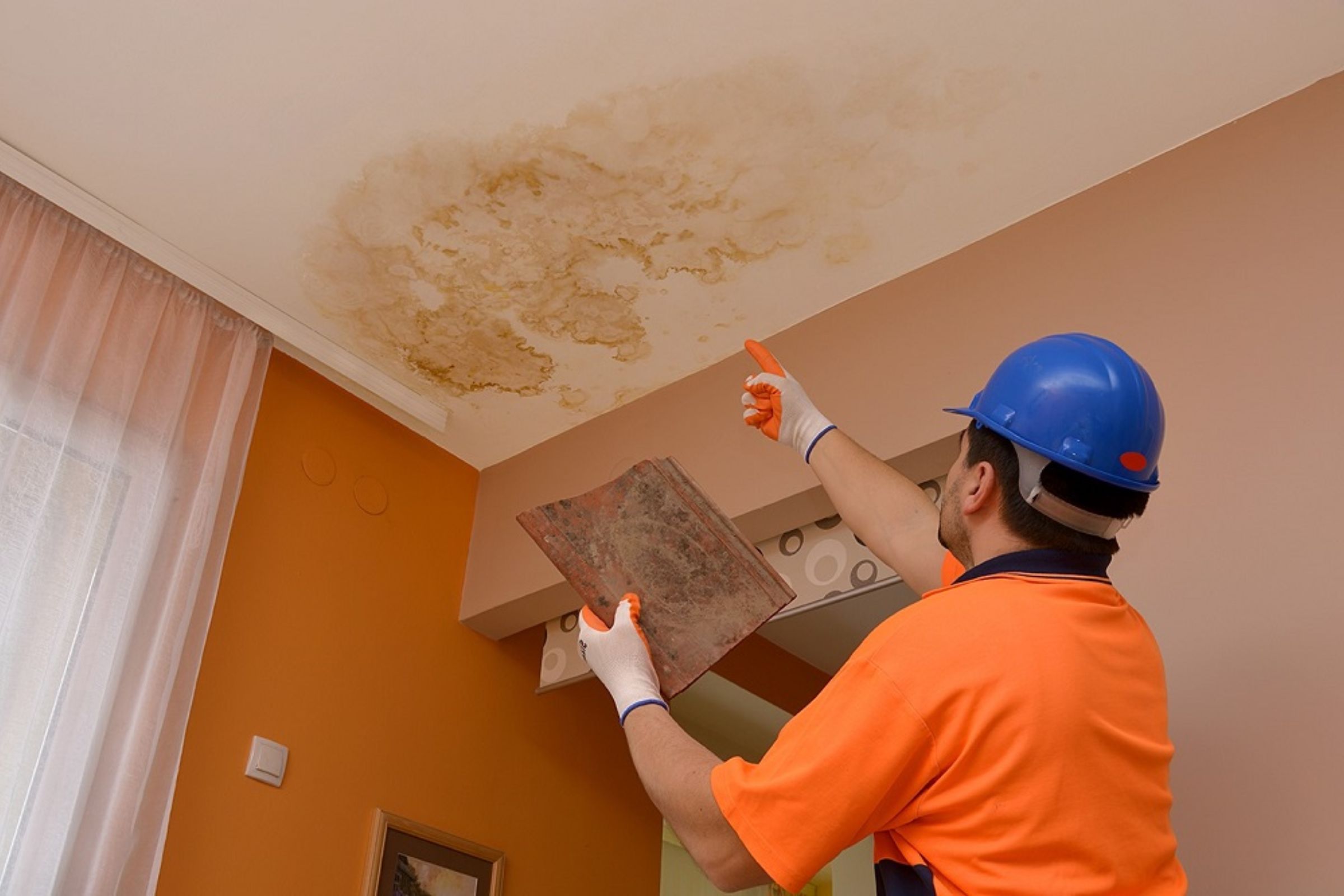 A man wearing an orange shirt and safety vest is holding a paper against the ceiling, indicating water damage restoration in Joliet, IL.