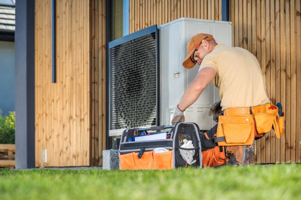 A man in a hard hat and work boots repairs an air conditioner, representing a mold removal service in action