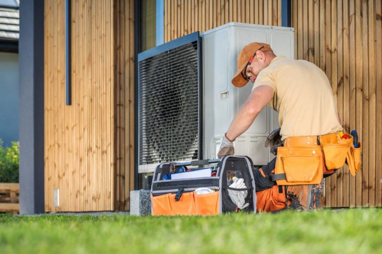 A man in a hard hat and work boots repairs an air conditioner, representing a mold removal service in action