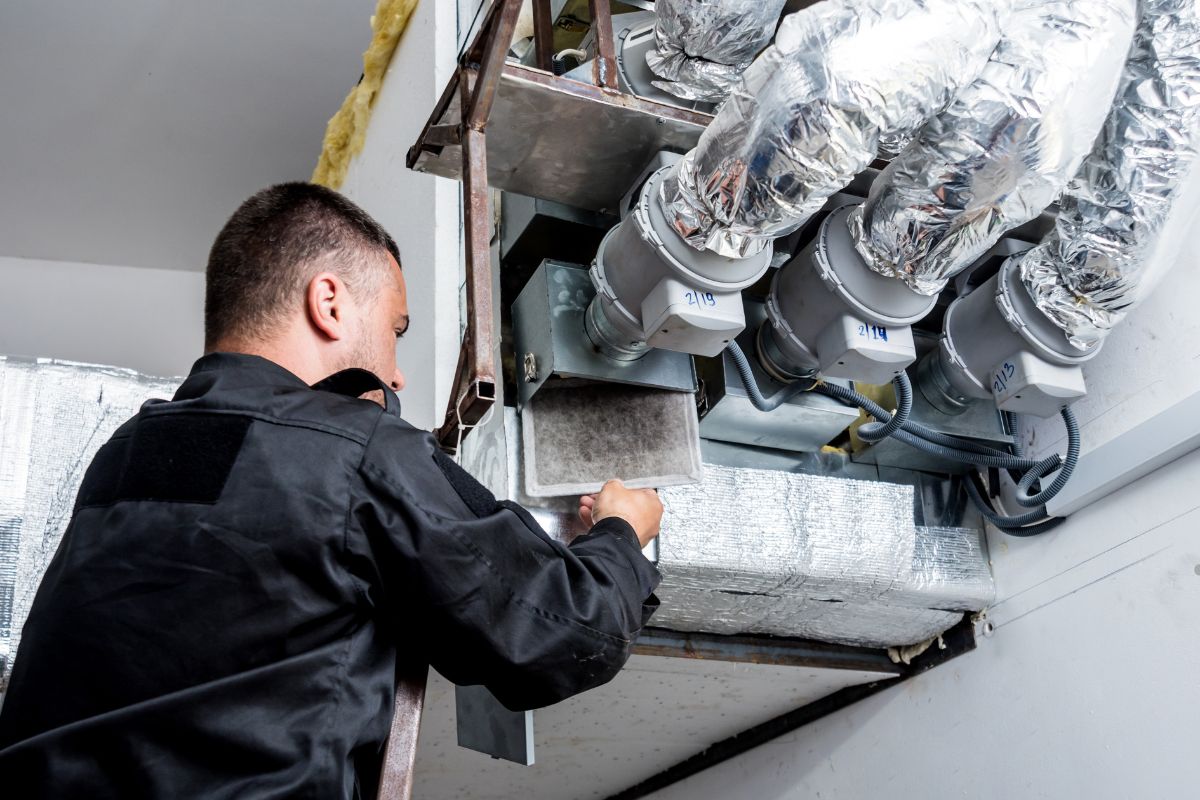 A man in a black shirt repairs a furnace, highlighting the importance of HVAC systems in preventing mold growth.